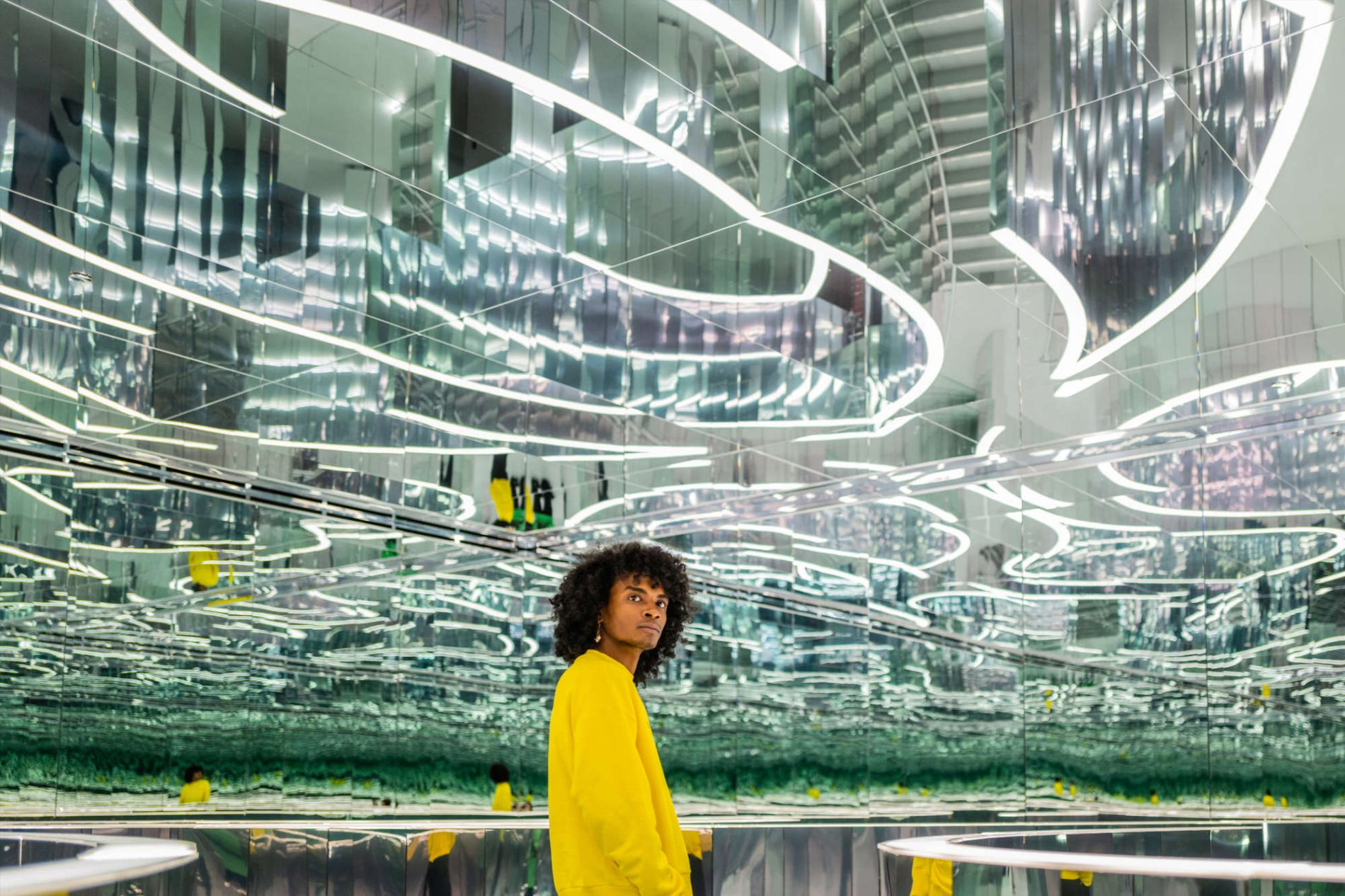 MAN STANDS AMIDST MIRRORS IN MIAMI’S IMMERSIVE ART MUSEUM CALLED SUPERBLUE IN INSTALLATION CALLED THE FOREST OF US